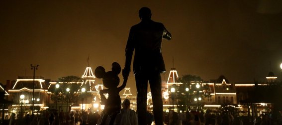 Disneyworld, FL. Mickey Mouse and Walt Disney statue in silhouette, buildings with open white festoon behind. Light fog and rain.